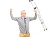 A happy gentleman patient holding crutches and gesturing happiness isolated against white background