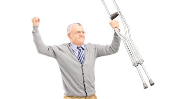 A happy gentleman patient holding crutches and gesturing happiness isolated against white background